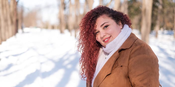 Portrait of a red-haired curly fat woman in the park in winter