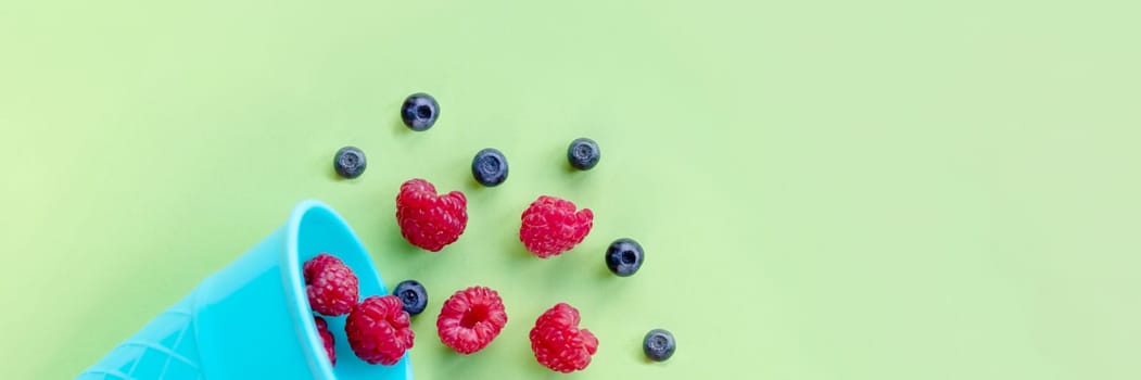 Waffle sweet ice cream cone with raspberries over white wooden background, top view.