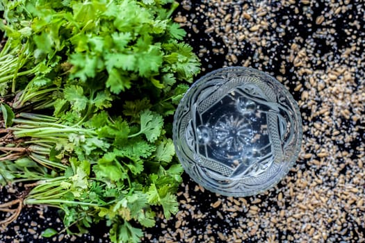 Exfoliating skincare face mask on a black-colored surface consisting of some coriander leaves and egg white along with some oats.