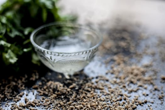 Exfoliating skincare face mask on a black-colored surface consisting of some coriander leaves and egg white along with some oats.