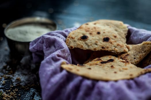 Shot of Gujarati breakfast consisting of round bread bhakri and lasun chutney. Shot of bhakhri, with wheat flour, garlic chutney, salt, ginger, and some whole wheat grains on a black glossy surface.