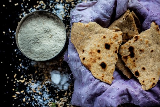 Shot of Gujarati breakfast consisting of round bread bhakri and lasun chutney. Shot of bhakhri, with wheat flour, garlic chutney, salt, ginger, and some whole wheat grains on a black glossy surface.