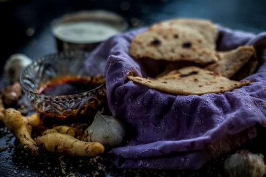 Shot of Gujarati breakfast consisting of round bread bhakri and lasun chutney. Shot of bhakhri, with wheat flour, garlic chutney, salt, ginger, and some whole wheat grains on a black glossy surface.