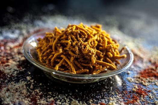 Diwali and Shravan Som special Teekha Gathiya in a glass plate along with some spread chickpea flour, red chili powder, and other ingredients that are needed to make the snack on a black surface.