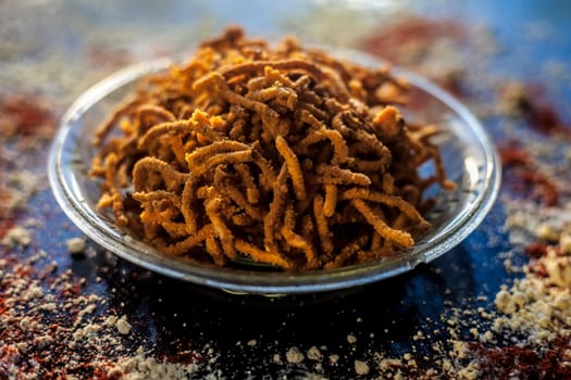 Diwali and Shravan Som special Teekha Gathiya in a glass plate along with some spread chickpea flour, red chili powder, and other ingredients that are needed to make the snack on a black surface.