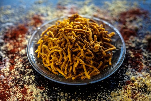 Diwali and Shravan Som special Teekha Gathiya in a glass plate along with some spread chickpea flour, red chili powder, and other ingredients that are needed to make the snack on a black surface.