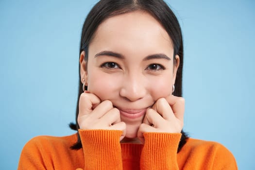 Beauty and wellbeing. Close up portrait of young happy asian woman, smiling and showing candid emotions, standing over blue background.