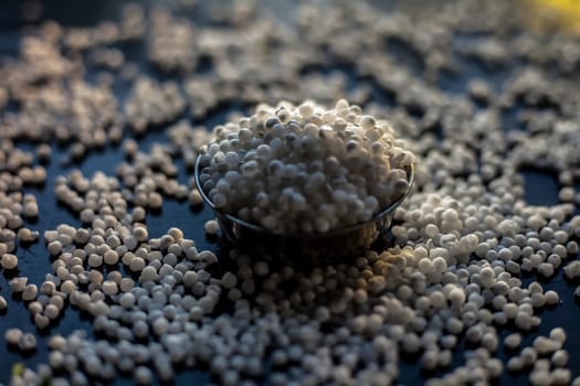 Close-up shot of raw sago pearls or tapioca pearls in a glass plate on a black-colored surface.