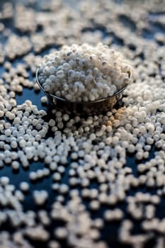 Close-up shot of raw sago pearls or tapioca pearls in a glass plate on a black-colored surface.