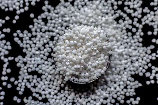 Close-up shot of raw sago pearls or tapioca pearls in a glass plate on a black-colored surface.