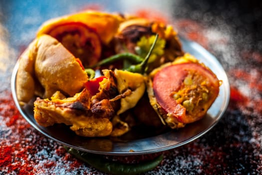 Shot of Indian tomato fritter on a glass plate along with some species on a black table. Shot of tomato pakora or tomato pakoda on a glass plate.