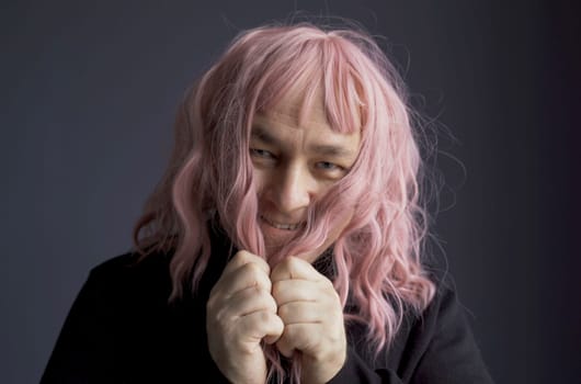 Portrait of a man who tried on a pink wig, looks at the camera, grimaces, poses. Close-up.