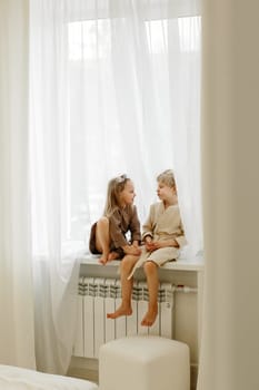 A boy and a girl in bathrobes are sitting on the windowsill, talking, playing.