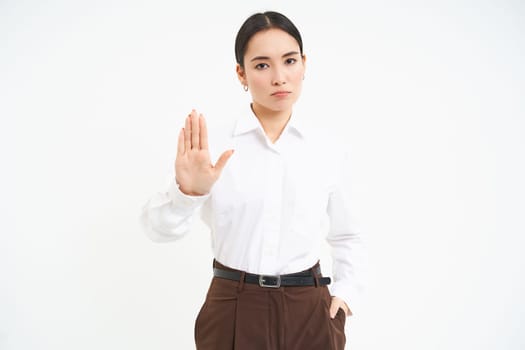 Stop. Strict and serious lady boss, asian woman shows extended hand, rejection, prohibit gesture, white background.