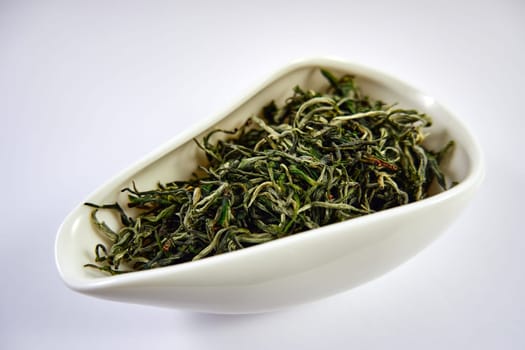 Dry Chinese green tea in a white porcelain bowl. Selective Focus