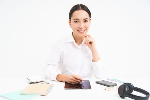 Young businesswoman sits in her office and writes on digital tablet, working in her company, isolated on white background.