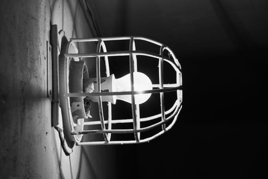 Glowing incandescent lamp. Old electric light bulb with a metal grate on the wall