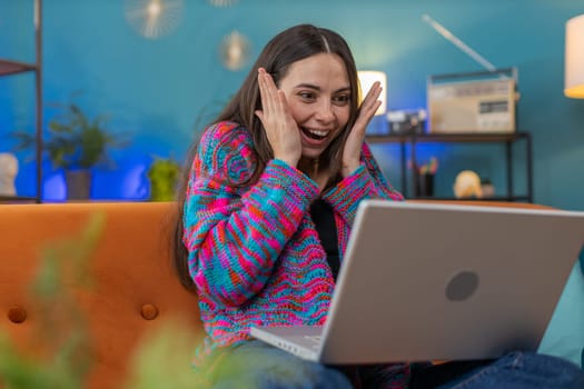 Surprised Caucasian woman using laptop computer, receive mail good news message, shocked by sudden victory celebrate lottery jackpot win purchases online shopping at home apartment on sofa. Lifestyles