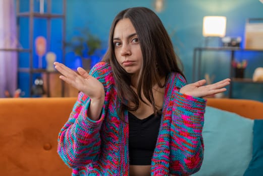 I dont know what to say. Confused young woman feeling embarrassed about ambiguous question, having answer doubts, no idea, being clueless and uncertain. Portrait of girl at home apartment room on sofa