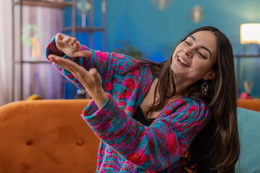 Cheerful rich young woman showing wasting or throwing money around hand gesture, more tips earnings, big profit, win lottery, body language, share. Portrait of girl at home apartment room on sofa