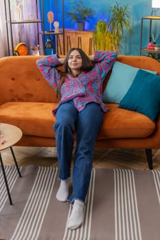 Tired woman lying down on comfortable couch taking a rest daytime nap. Portrait of carefree young girl holding hands behind head relaxing falling asleep at home apartment living room on sofa. Vertical