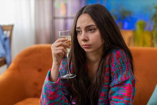 Sad young woman girl sitting at home looks pensive of unrequited love, suffers from unfair situation, drinking champagne, bad news. Problem break up, depressed feeling bad annoyed, burnout, bankruptcy