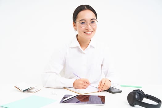 Office work and business. Young professional female employer, team leader sitting at workplace with digital tablet, smiling at camera, white background.