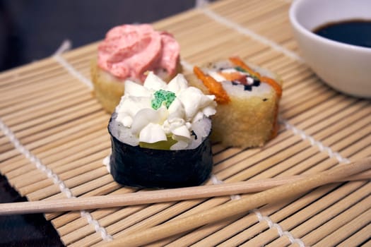 Sushi, chopsticks and a bowl of soy sauce on a bamboo mat