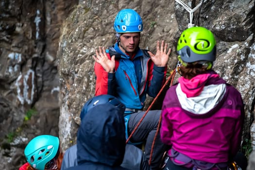 A man, instructor explains to students how to behave in the mountains, a group of people are trained in mountaineering techniques in a camp outdoor on the cliffs.