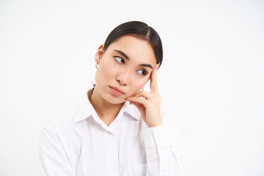Portrait of annoyed, bored korean woman roll eyes, looks aside with bothered, tired face expression, stands over white background.
