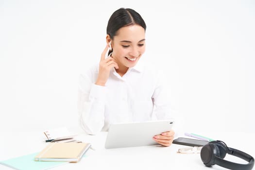 Portrait of korean businesswoman in headphones, connects to meeting on digital tablet, talks on video chat, joins online conference, white background.