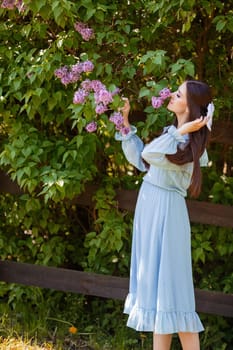romantic beautiful girl in light blue dress stands in the garden, nearby blooming lilac bush , in sunny day. Close up. Vertical. copy space