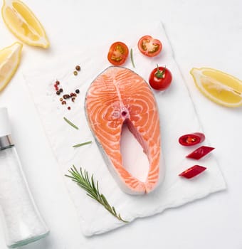 Raw piece of salmon, lemon slices and spices on a white board, top view