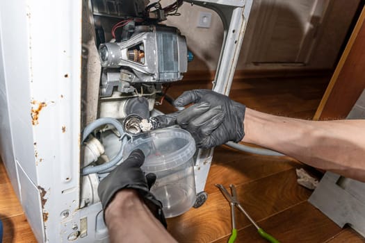 A repairman repairs a used washing machine. The water pump and rubber hoses are clogged with sediments. A jammed pump. calcium-magnesium deposits. Scum