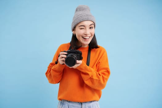 Passionate asian girl photographer, taking pictures on her digital camera, capturing moments outdoors, shooting photos, blue background.