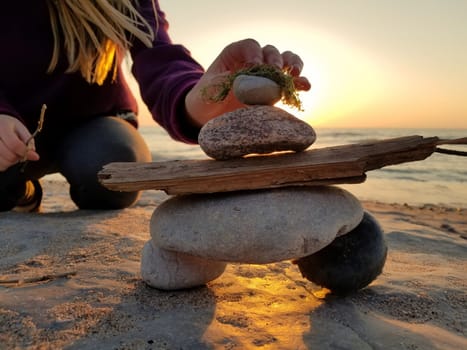 Young girl builds an inukshuk inuksuk with seaweed hair at the beach at sunset 2