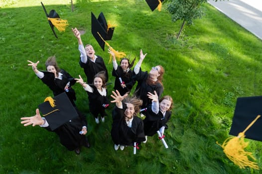 Classmates in graduation gowns throw their caps. View from above