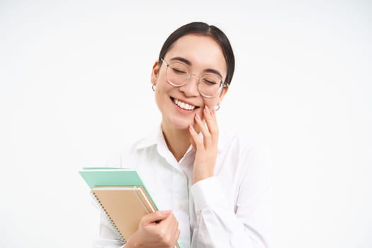 Successful young asian woman, teacher with notebooks, looking confident and smiling, white studio background.