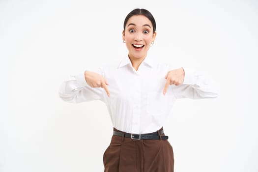 Confident smiling businesswoman, asian office lady points fingers down, shows advertisement, promo offer below, white background.