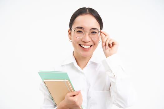 Smiling woman professional, asian female teacher with glasses, looking confident, standing over white background.