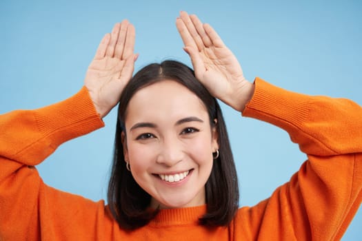 Close up of candid young female model laughs and smiles, shows natural happy emotions, stands over blue background.