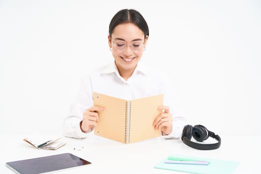 Image of hardworking student, asian woman in glasses studying, holding notebook, working on project, isolated over white background.