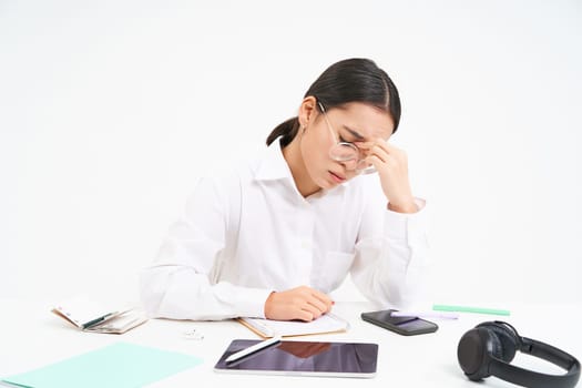 Workplace and business. Portrait of tired woman in office, company employee sits at desk with exhausted face, touches her head, has headache, white background.
