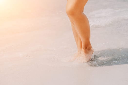 Sea beach travel - woman walking on sand beach leaving footprints in the white sand. Female legs walking along the seaside barefoot, close-up of the tanned legs of a girl coming out of the water