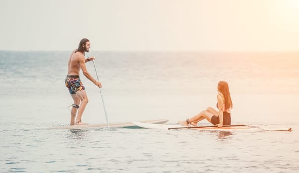Sea woman and man on sup. Silhouette of happy young woman and man, surfing on SUP board, confident paddling through water surface. Idyllic sunset. Active lifestyle at sea or river