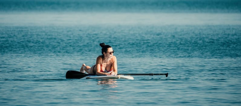 Silhouette of woman standing, surfing on SUP board, confident paddling through water surface. Idyllic sunset or sunrise. Sports active lifestyle at sea or river.