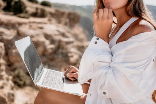 Digital nomad, Business woman working on laptop by the sea. Pretty lady typing on computer by the sea at sunset, makes a business transaction online from a distance. Freelance remote work on vacation