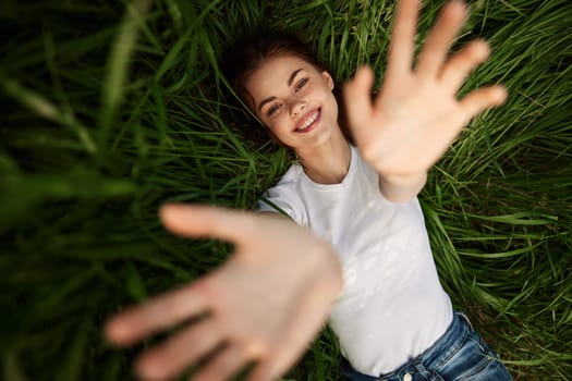 laughing redhead woman stretching her palms to the camera while lying on the grass. High quality photo