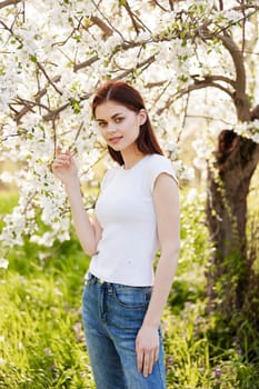 portrait of a happy woman with red hair in casual clothes enjoying the flowering of a fruit tree. High quality photo