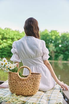 a woman with well-groomed hair is resting on the pier sitting with her back to the camera enjoying nature. High quality photo